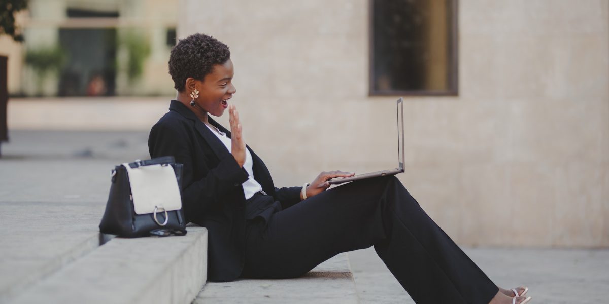 Stylish black woman with laptop on steps near handbag